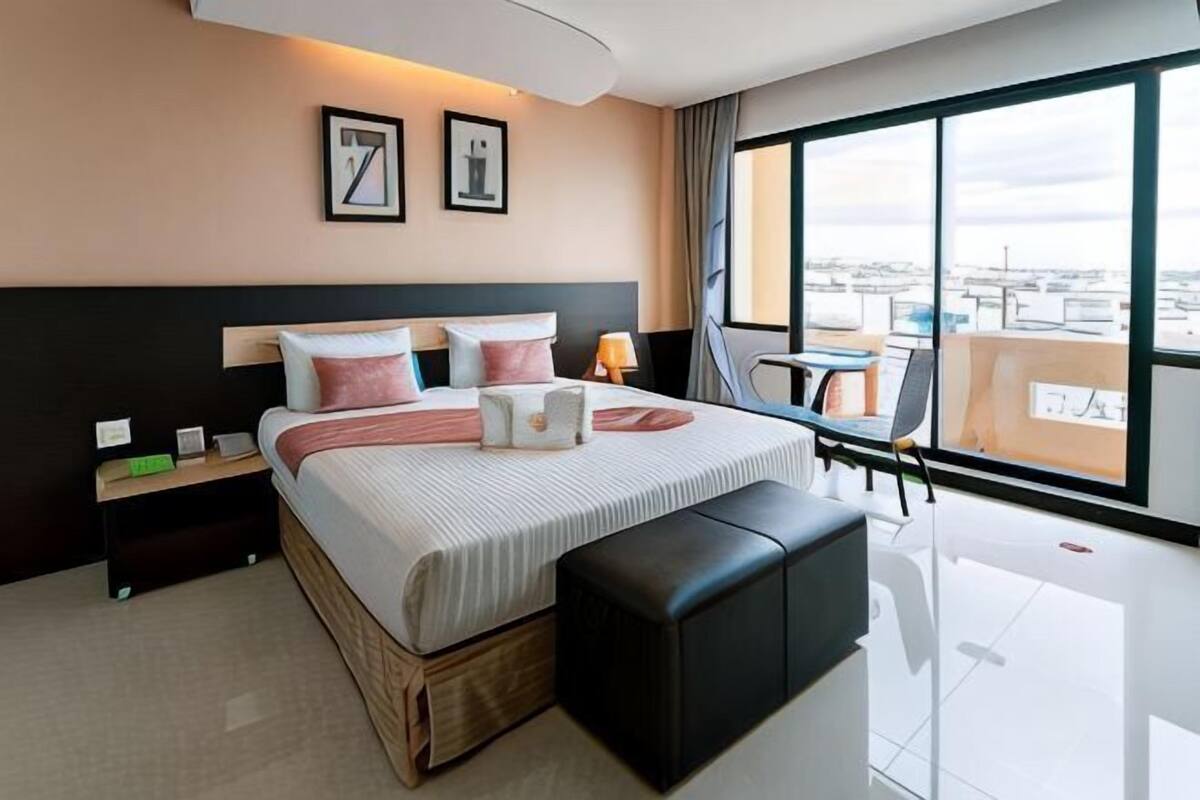 Una habitación de hotel moderna con una cama grande, una mesita de noche, un escritorio pequeño, una silla y un ventanal con vistas a la ciudad.