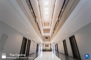 Een moderne hotelgang met een centrale trap, meerdere deuren en een receptie aan het einde.