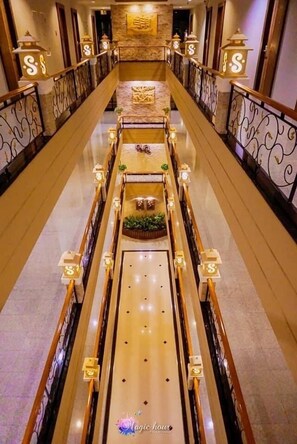 Pasillo de hotel con un pasillo central, barandillas decorativas y señalización iluminada.