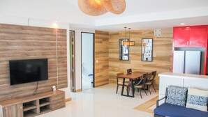 Un salon moderne doté d’un téléviseur à écran plat, de lambris en bois, d’un coin repas avec une table et des chaises, et d’une cuisine rouge avec un réfrigérateur.