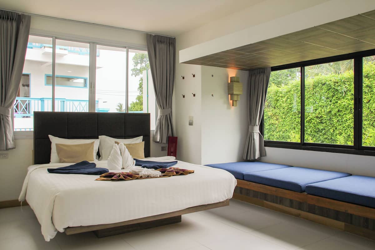 A modern bedroom with a large bed, a built-in bench, and a view of greenery outside.