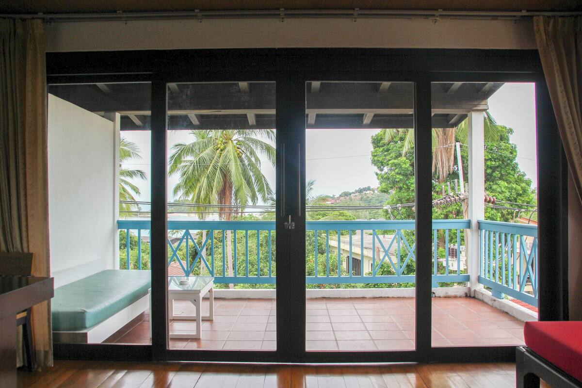 A room with a sliding glass door leading to a balcony with a blue railing and a bench.