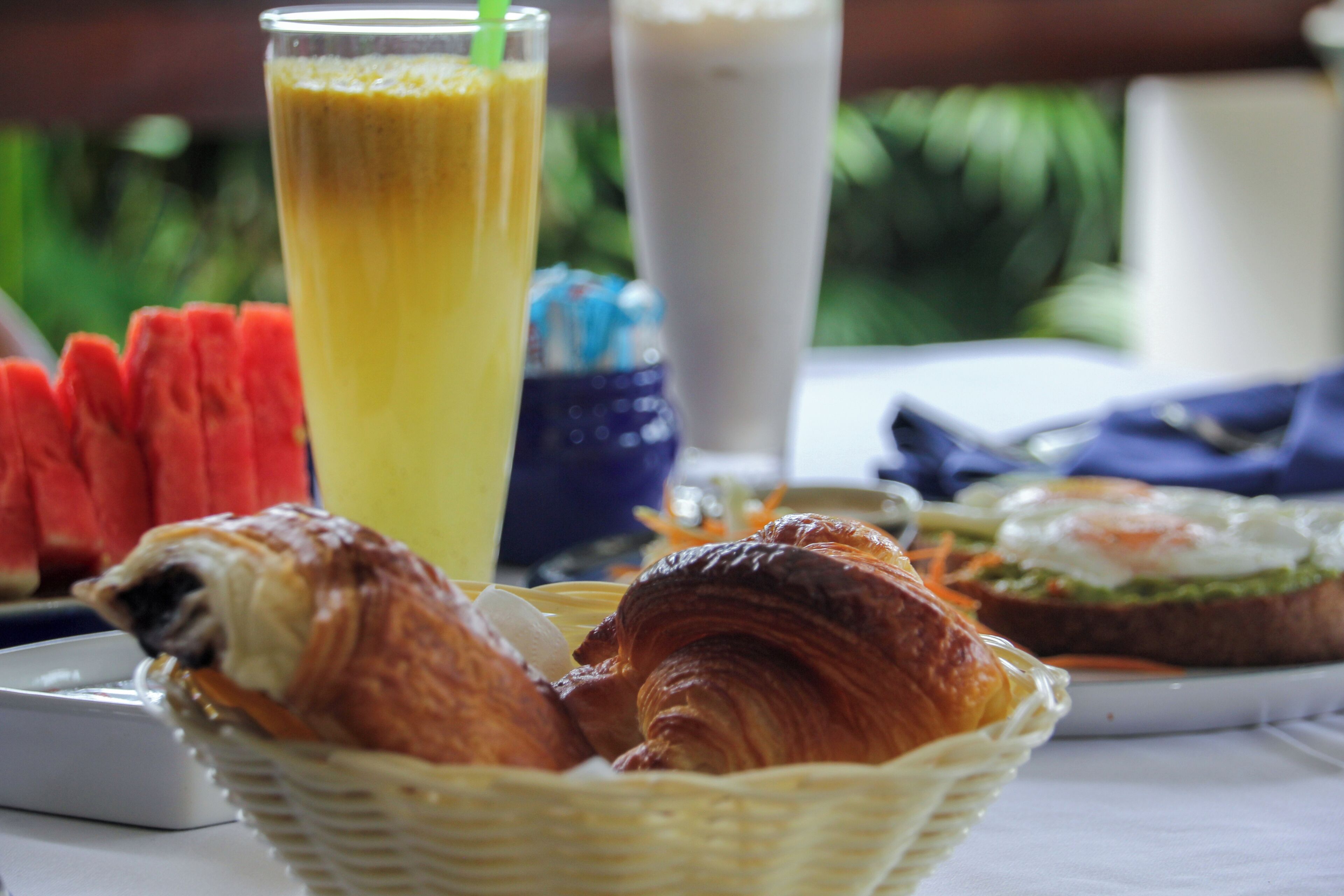 Una mesa con croissants, un vaso de zumo de naranja, un batido y un plato de sandía en rodajas.