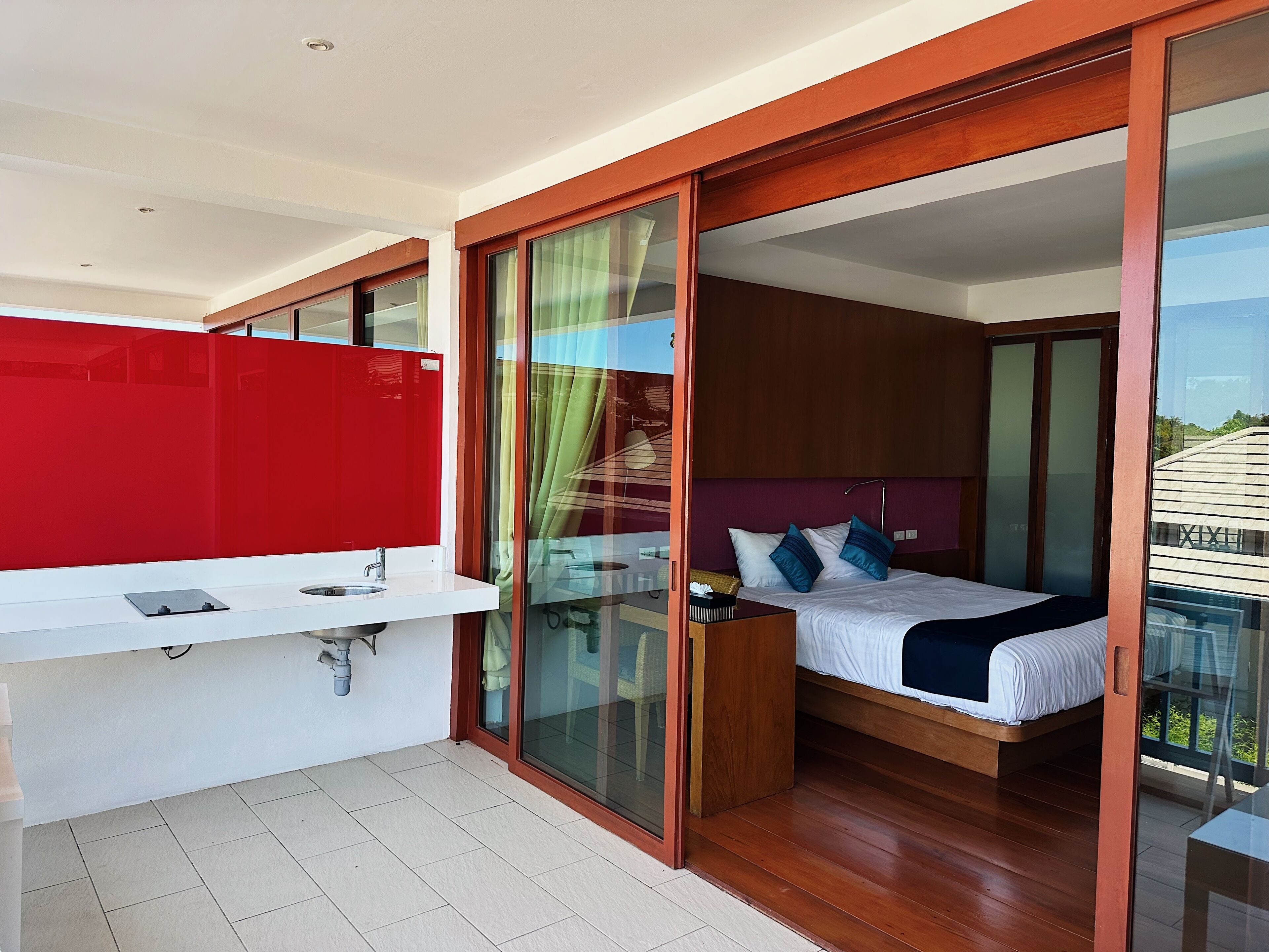 A modern bedroom with a bed, a bedside table, a red partition, and a bathroom with a sink and mirror.