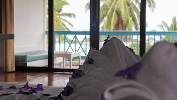 Une chambre avec un lit, une vue sur des palmiers et un balcon doté d’une balustrade bleue.