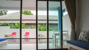 Une chambre moderne dotée d’une porte-fenêtre coulissante donnant sur un espace extérieur avec une piscine, des fauteuils de relaxation rouges et une table blanche.