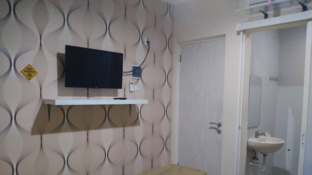 Ein Zimmer mit einem Bett, einem an der Wand befestigten Fernseher, einem Badezimmer mit einem Waschbecken und einer Tür.