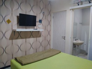 A room with a bed, a mounted TV, a bathroom with a sink, and a door. - Budget Guest House Tunas Mandiri Jaya (Malang)