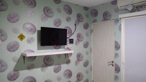Ein Zimmer mit Fernseher auf einem weißen Regal, Wandtapete mit Muster, einer Tür und einem „RAUCHVERBOT“-Schild.