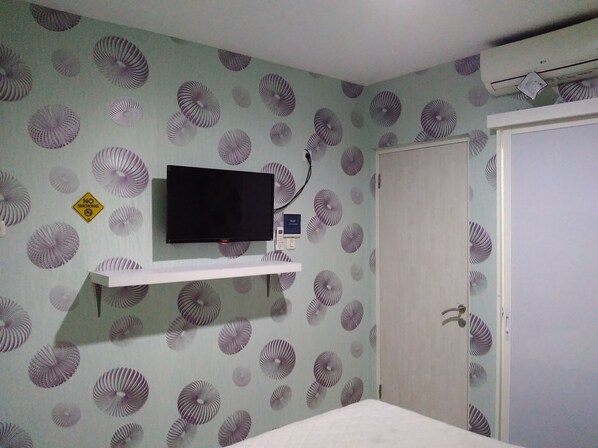 A room with a television on a white shelf, patterned wallpaper, a door, and a "NO SMOKING" sign. - Budget Guest House Tunas Mandiri Jaya (Malang)