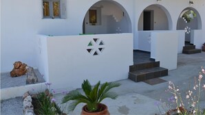 A white building with arched doorways and a central staircase leading to an upper level. - Kochylas Studios (Skiros)