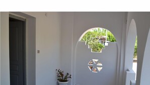 A hallway with a white door, a potted plant, and a decorative cut-out window. - Kochylas Studios (Skiros)