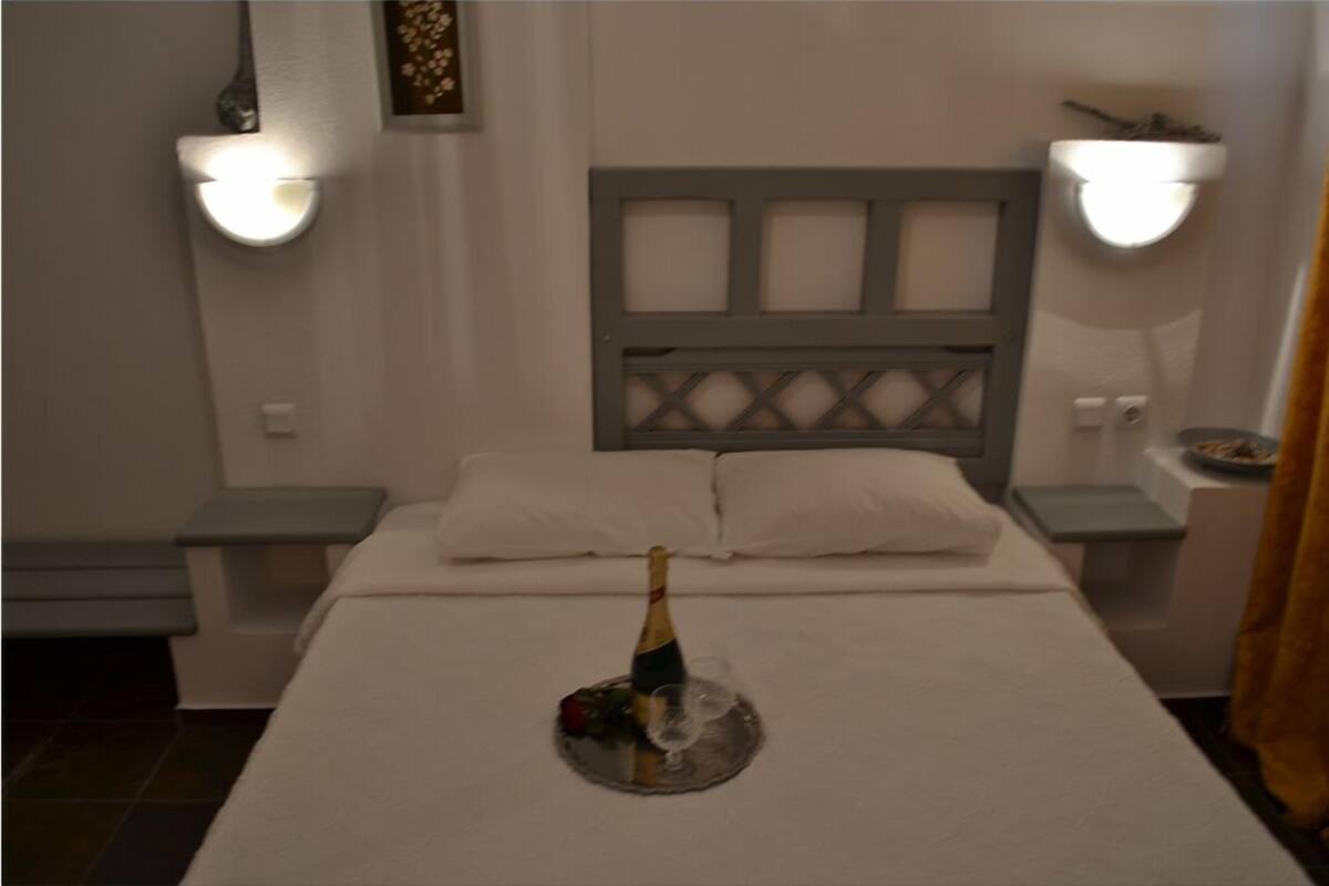 A bedroom with a bed, nightstands, a headboard, and wall-mounted lights.
