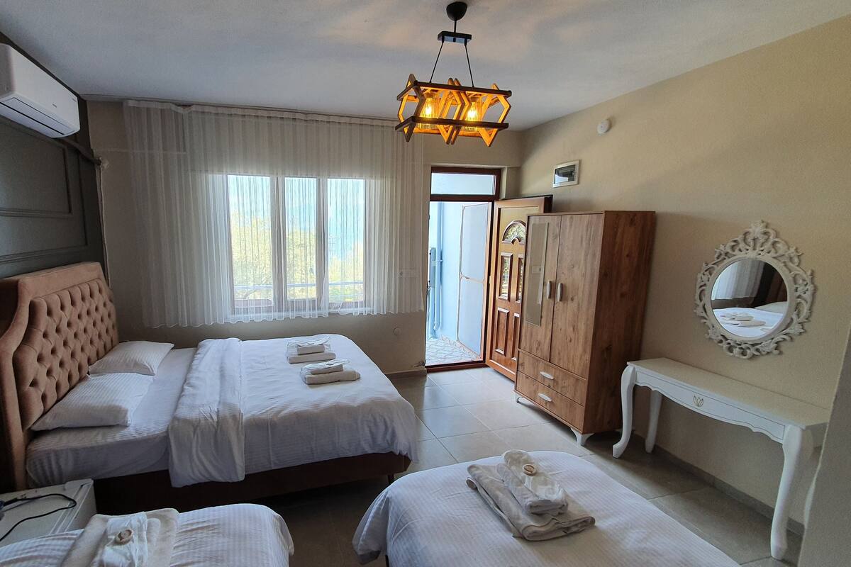 A hotel room with two beds, a wooden wardrobe, a bedside table, a mirror, and a window with curtains.