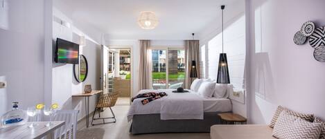 A modern hotel room with a bed, a desk with a computer, a chair, and a view of the outdoors.
