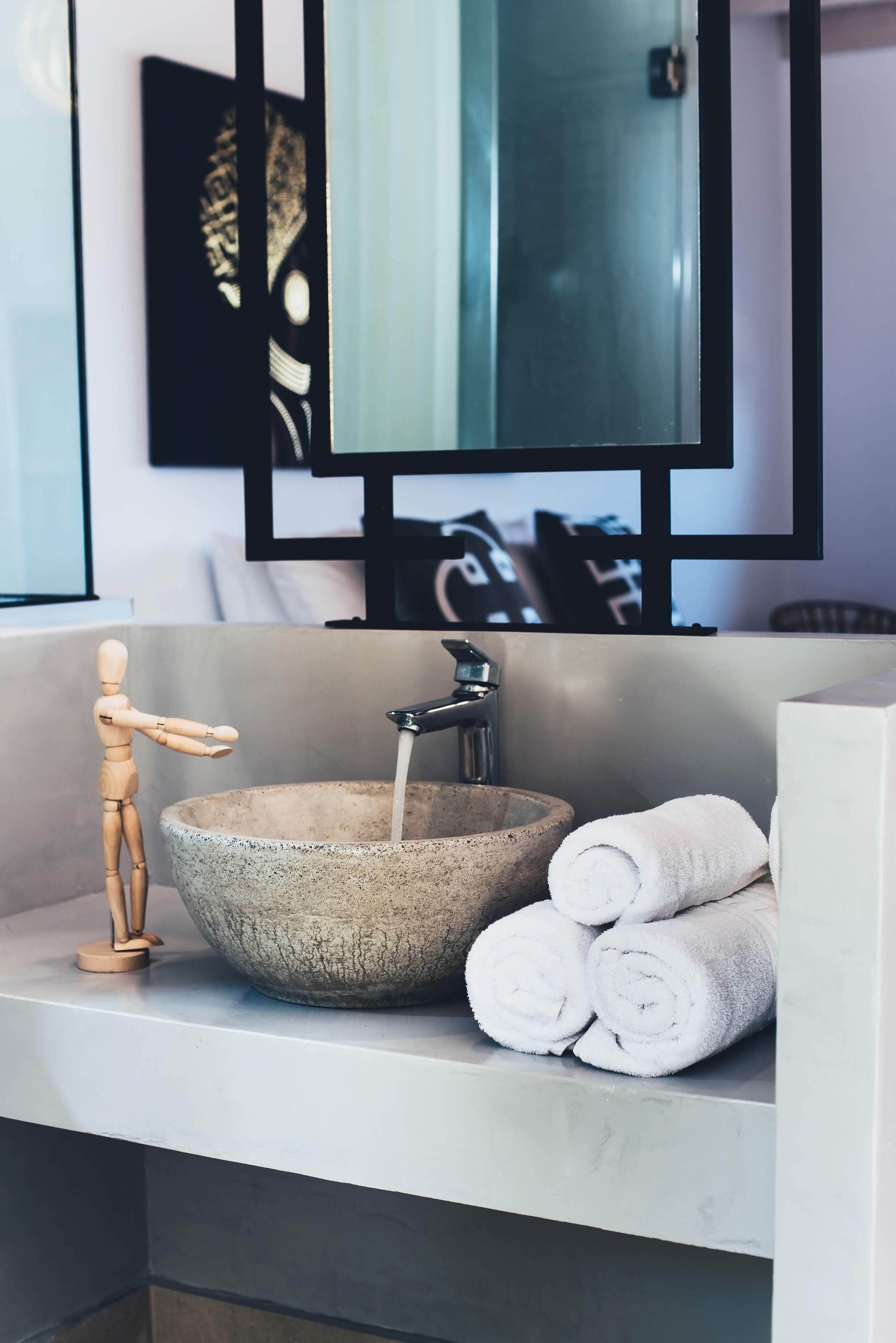 A bathroom with a stone sink, a wooden mannequin, and rolled towels.
