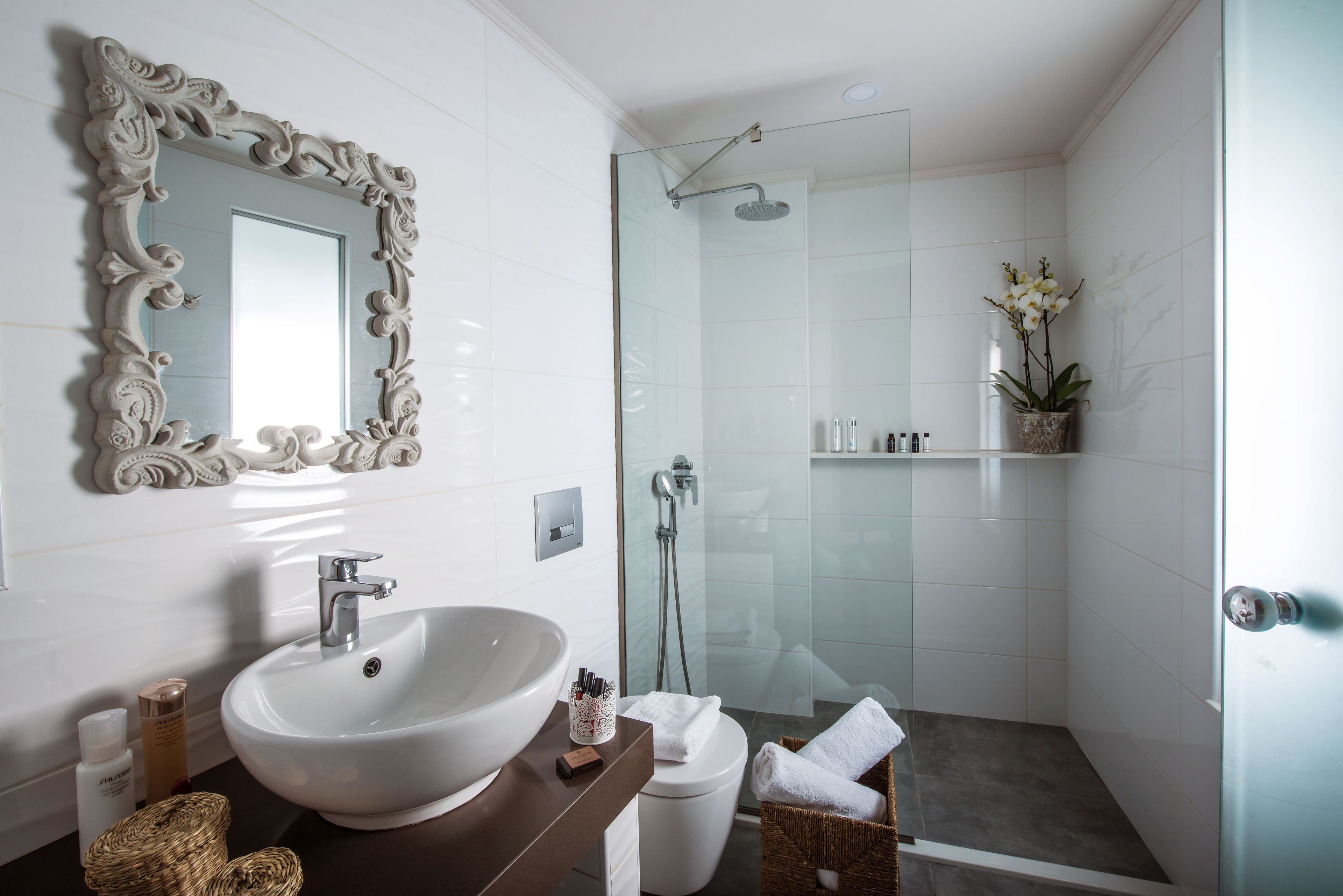 A bathroom with a white sink, a mirror with ornate detailing, a shower area, and a towel basket.