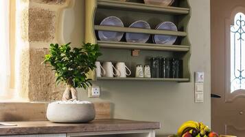 A kitchen with a built-in shelf holding plates and cups, a potted plant on the counter, and a fruit bowl on the table.