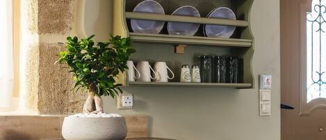 A kitchen with a built-in shelf holding plates and cups, a potted plant on the counter, and a fruit bowl on the table.