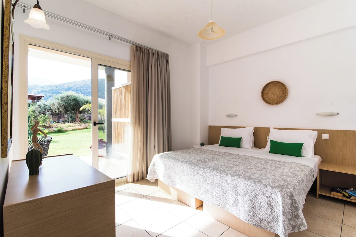 A hotel room with a bed, a desk, a view through a glass door, and a ceiling light.