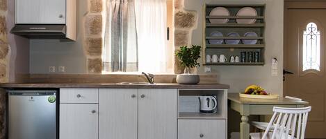 A compact kitchen with a built-in dishwasher, a window with curtains, a potted plant, and a dining area with a table and chairs.