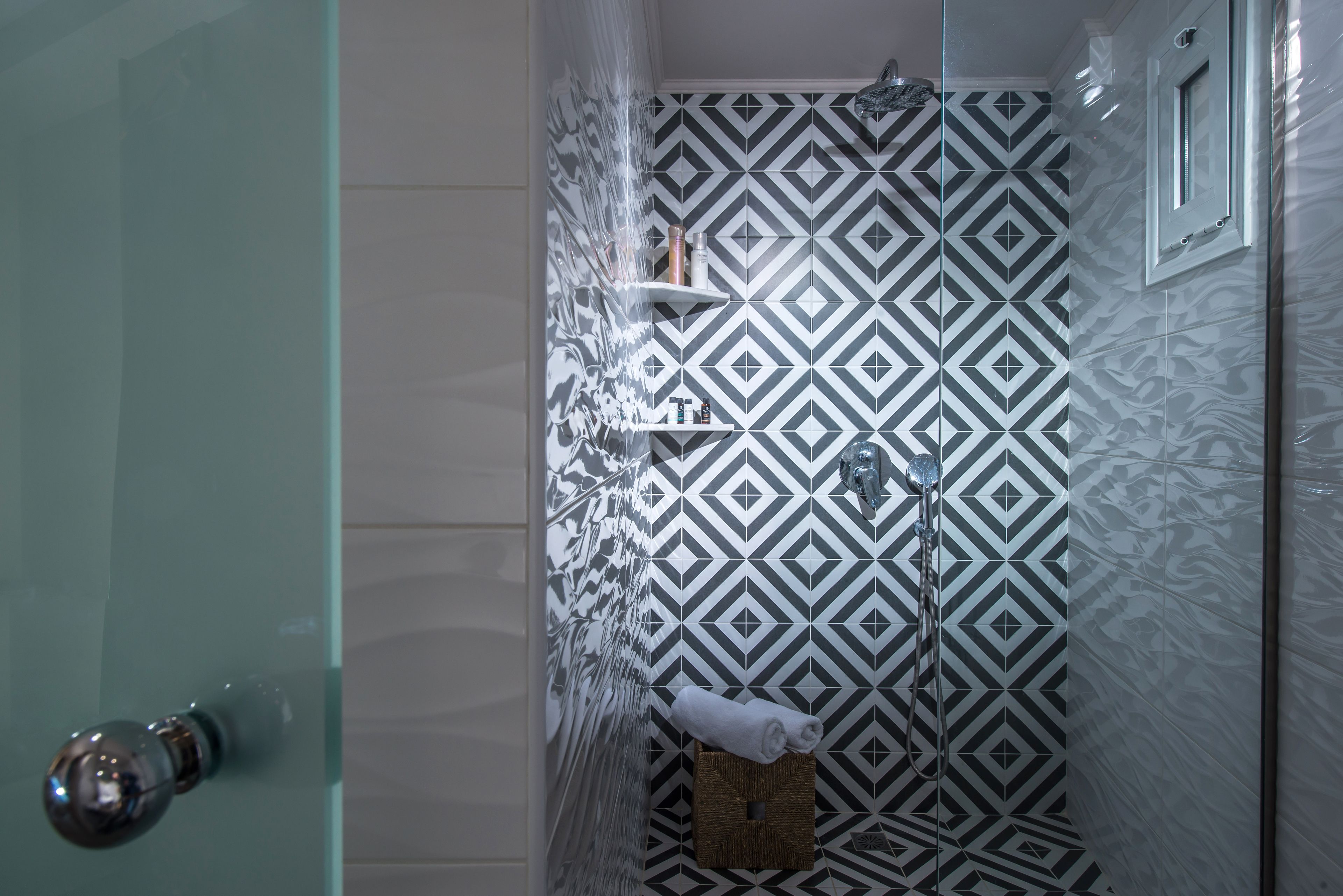 A shower with a geometric patterned wall, a glass door, and a towel on the floor.