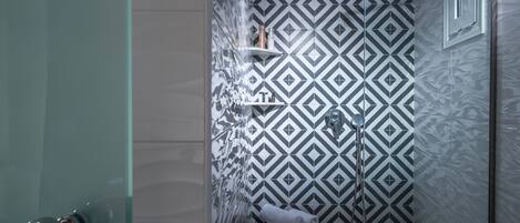 Ducha con pared de diseño geométrico, puerta de cristal y una toalla en el suelo.