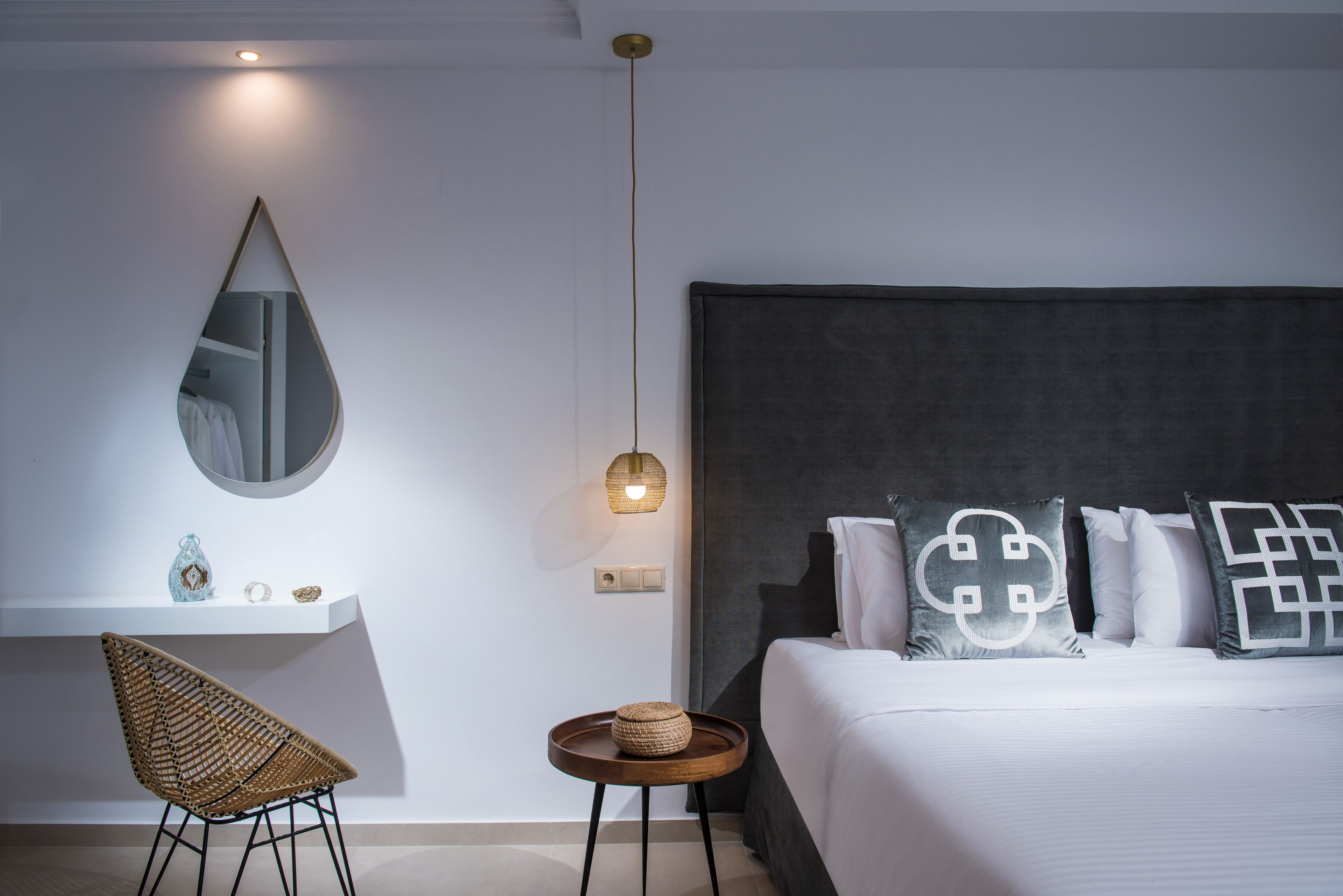 Un dormitorio moderno con cama, una mesita de noche, una silla, un espejo y una lámpara colgante.