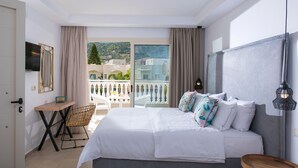 Quarto de hotel com cama, escrivaninha, cadeira, televisão e varanda com vista para edifícios e árvores.