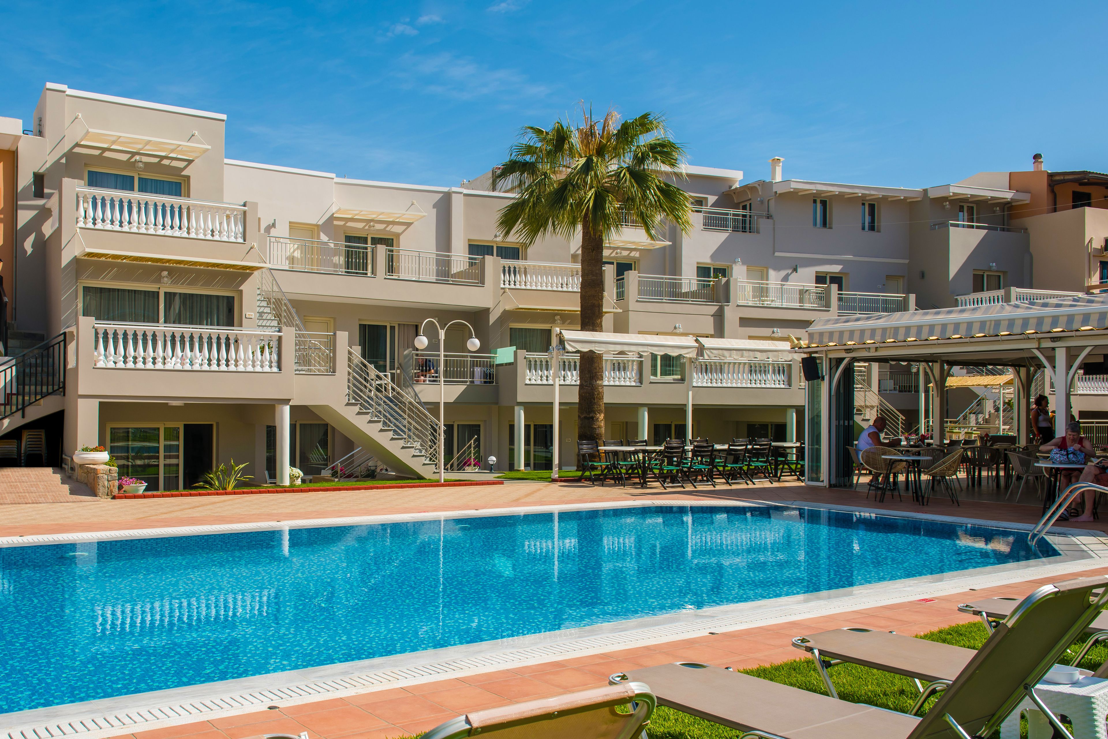 A hotel with a swimming pool, outdoor seating, and a palm tree.
