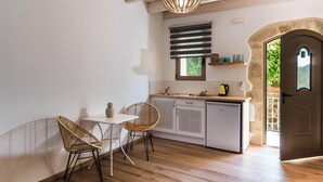 Uma cozinha com bancada branca, duas cadeiras de vime, luminária pendente e porta que dá para o exterior.