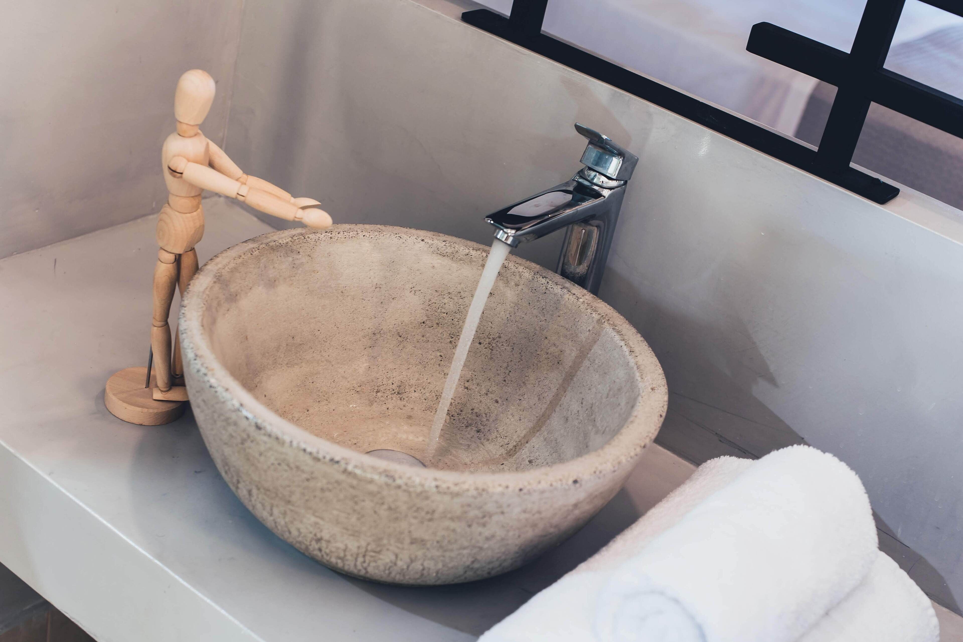 A bathroom with a large stone sink, a wooden mannequin, and a towel.