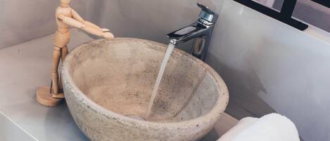 A bathroom with a large stone sink, a wooden mannequin, and a towel.