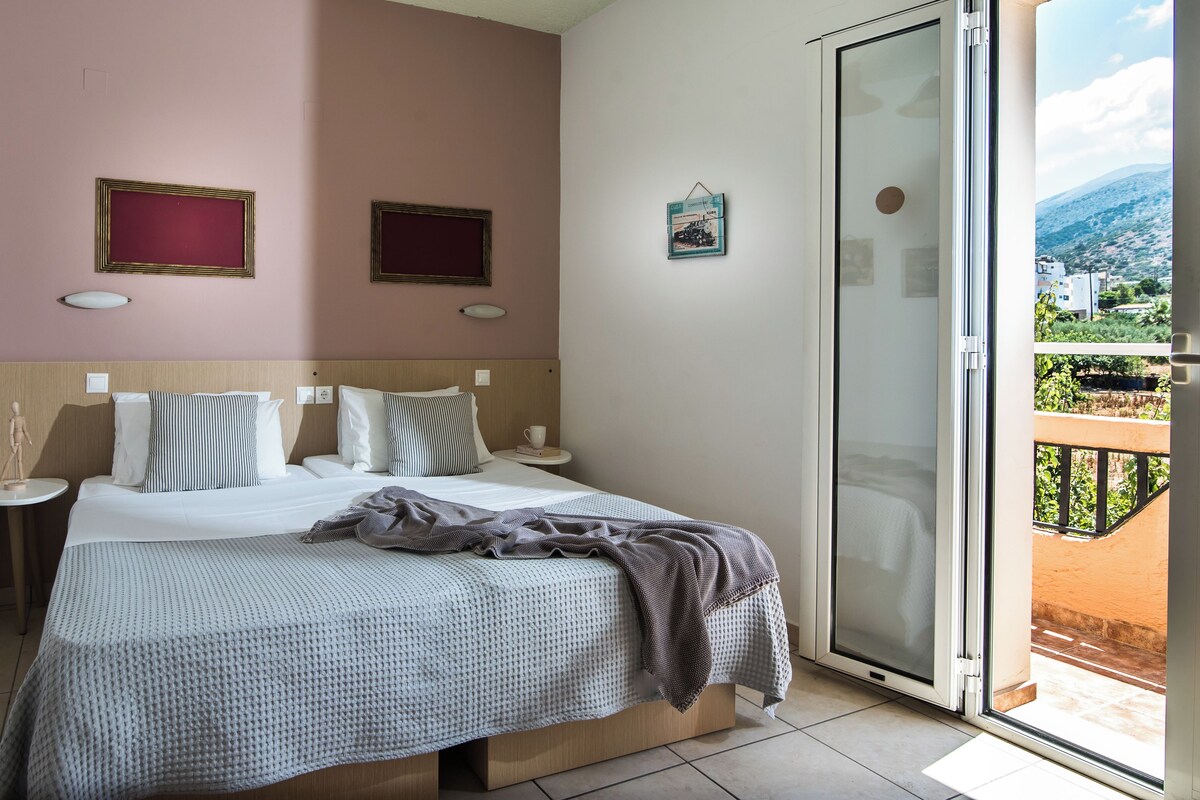 Un dormitorio con cama, mesitas de noche, una ventana con vistas y adornos en las paredes.