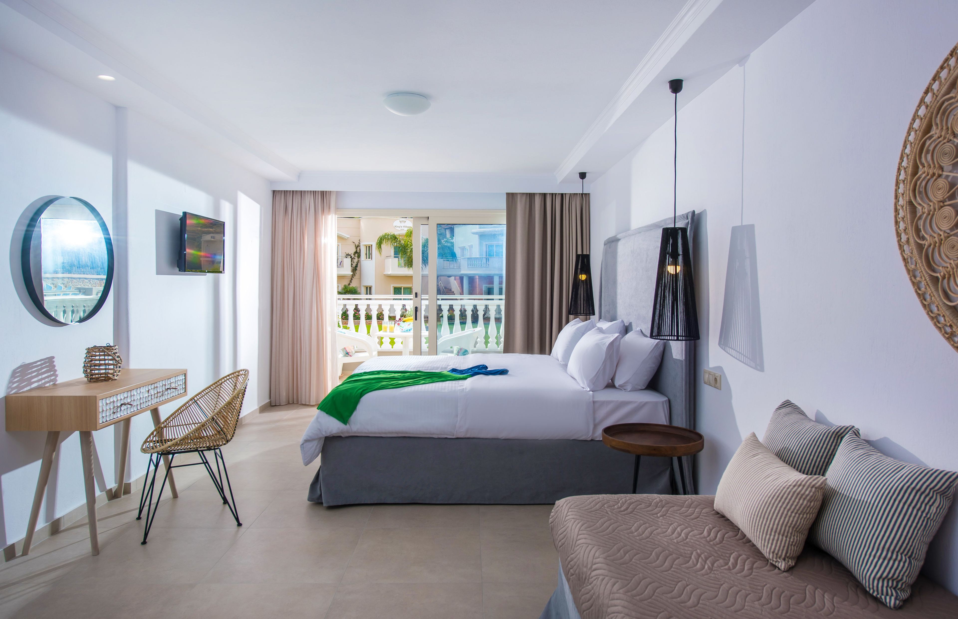 A hotel room with a bed, a desk, a chair, a balcony with a view, and a large mirror.