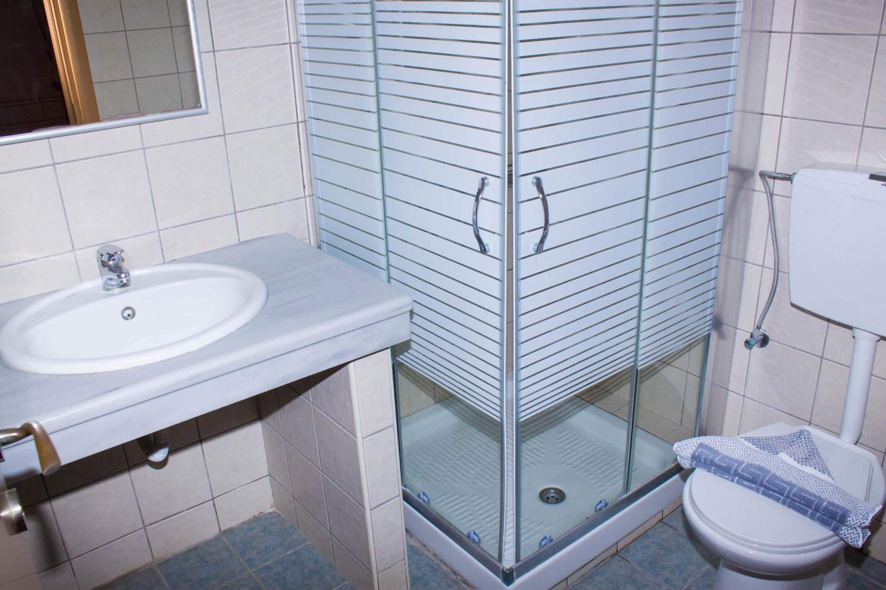 A bathroom with a glass-enclosed shower, a white sink, and a toilet.