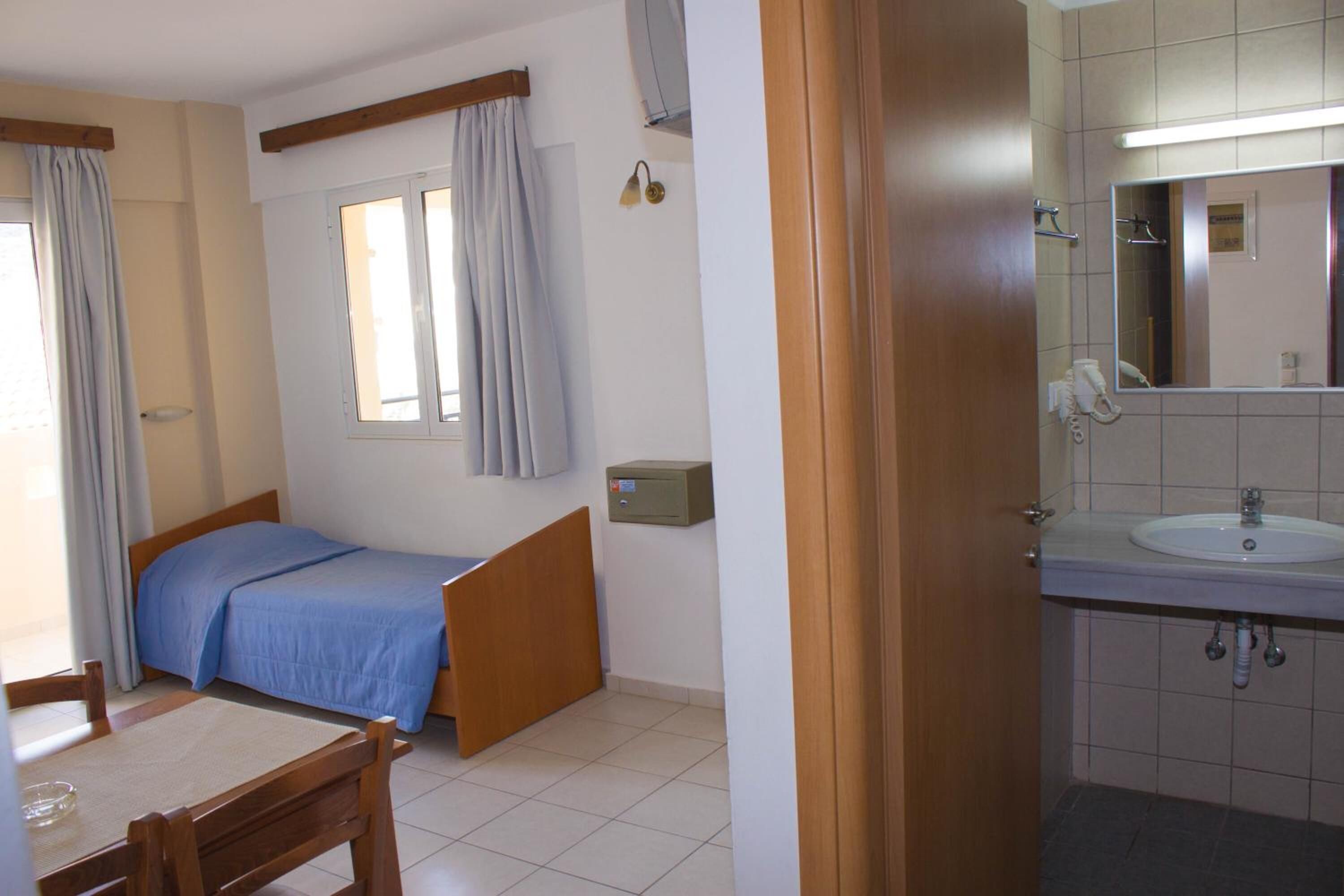 A bedroom with a single bed, a window, a bedside table, and a small cabinet.