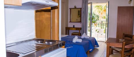 A compact hotel room with a kitchenette, a bed with blue bedding, a small table, and a chair.