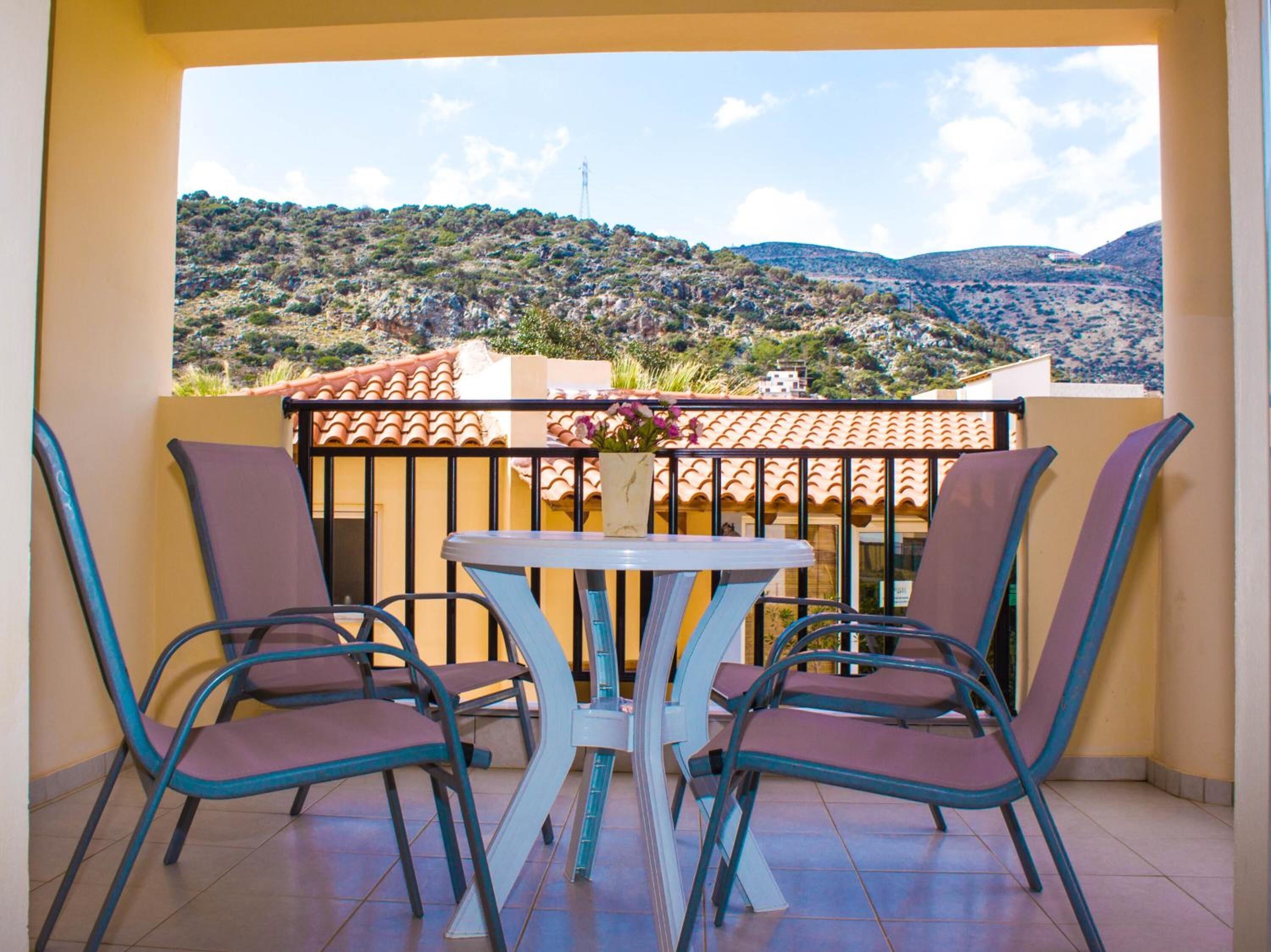 A balcony with a table and chairs, offering a view of a hilly landscape.