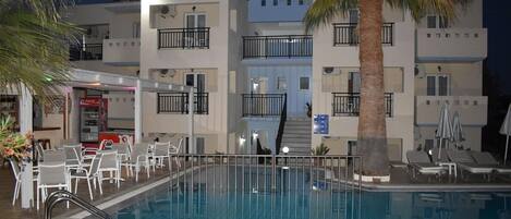 A hotel with a swimming pool, outdoor seating, and palm trees.