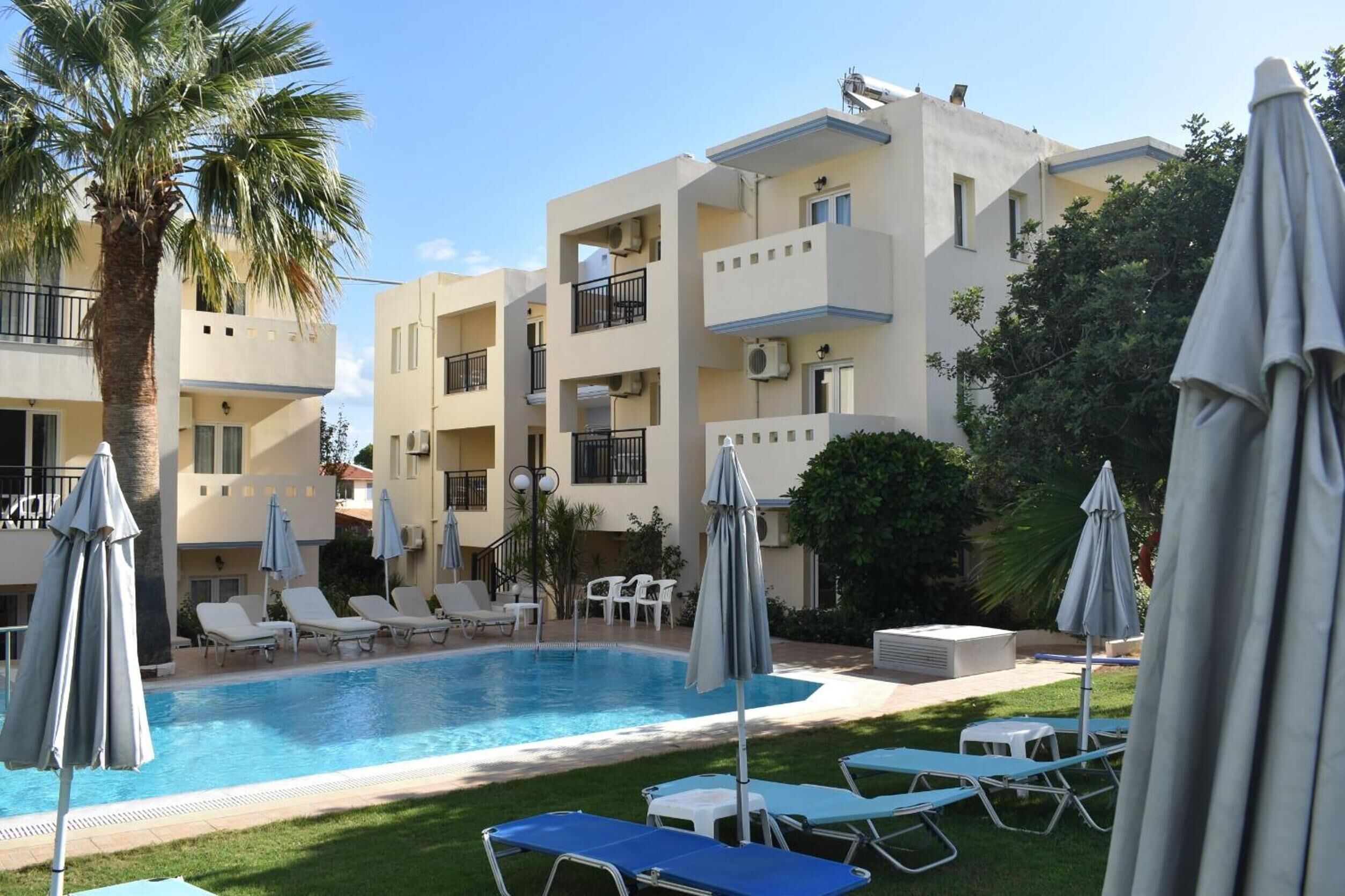 A pool area with lounge chairs and umbrellas, surrounded by a multi-story building with balconies.