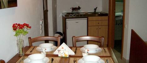 Un coin repas avec une table dressée pour quatre personnes, un petit réfrigérateur et des placards en bois.