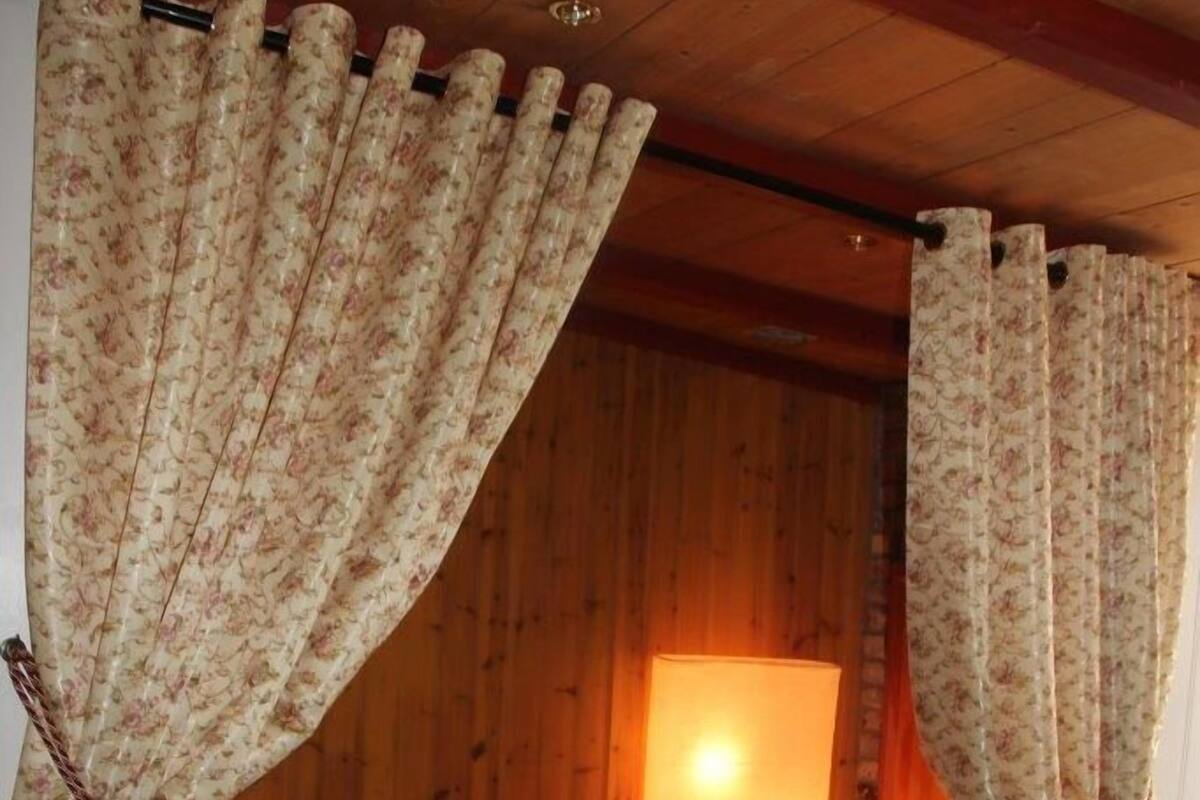 A cozy room with a bed, floral curtains, and a wooden ceiling.
