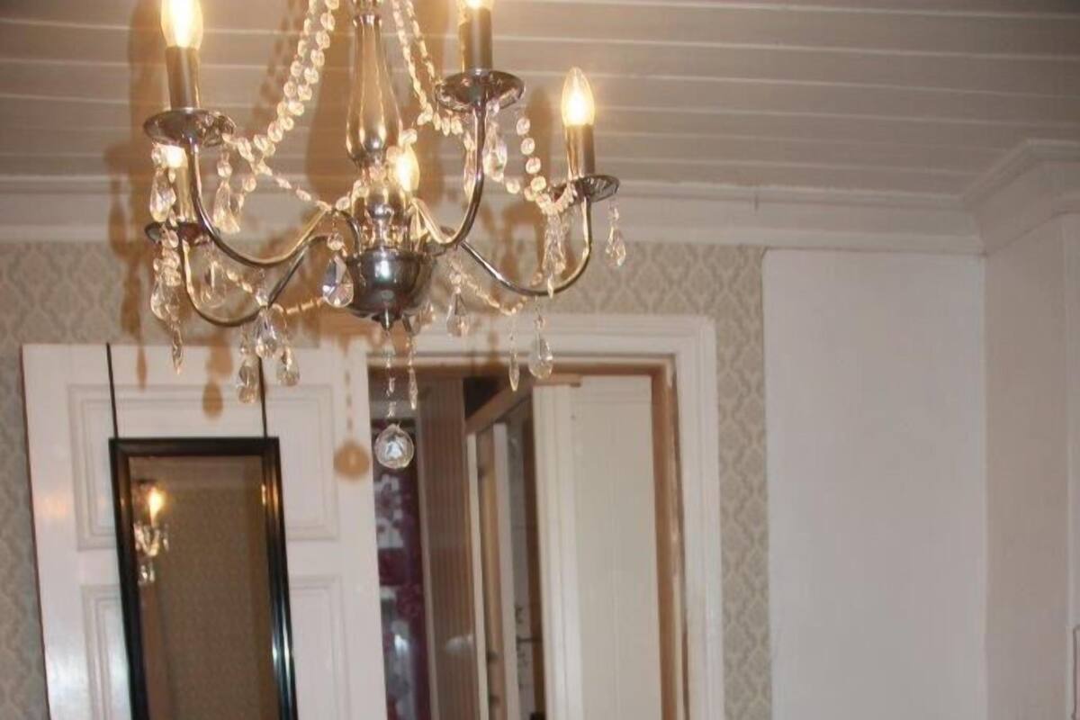 A bedroom with a bed, a chandelier, a chair, and a mirror.