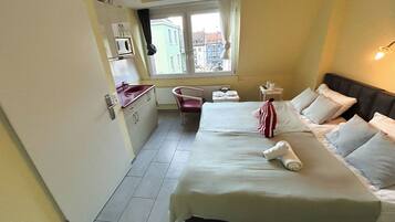 Une chambre d’hôtel de taille réduite, comprenant un lit, une table de chevet, une chaise et une kitchenette.