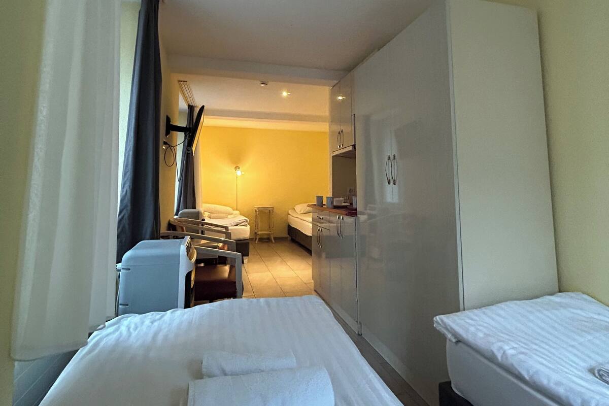 A hotel room with two beds, a desk, a chair, a wardrobe, and a small kitchenette.