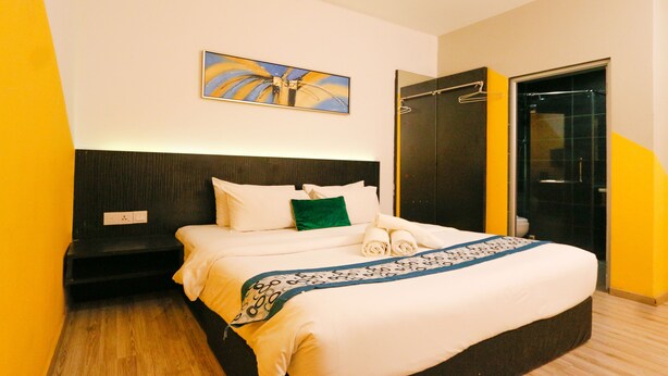 A neatly made bed with white linens and a blue patterned throw, a green pillow, and a painting above it. - Golden Roof Hotel Sunway Ipoh (Ipoh)