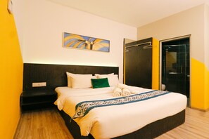 Una cama bien hecha con sábanas blancas y un plaid azul estampado, una almohada verde y un cuadro en la pared de encima.
