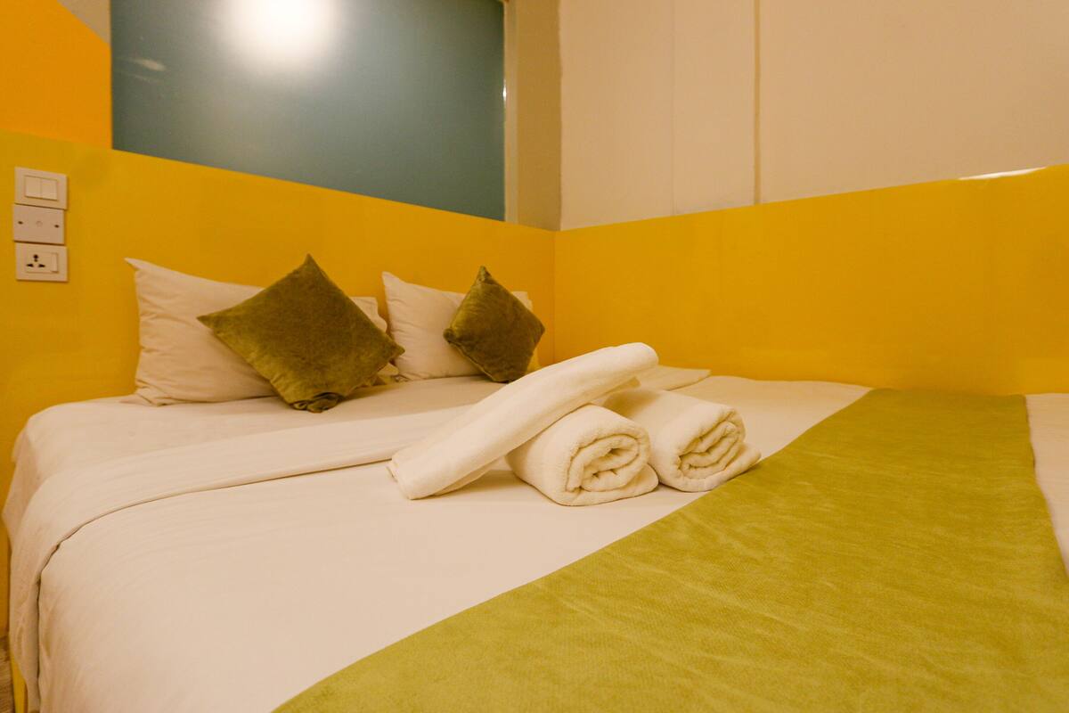 A hotel room with a bed, pillows, and a green blanket.