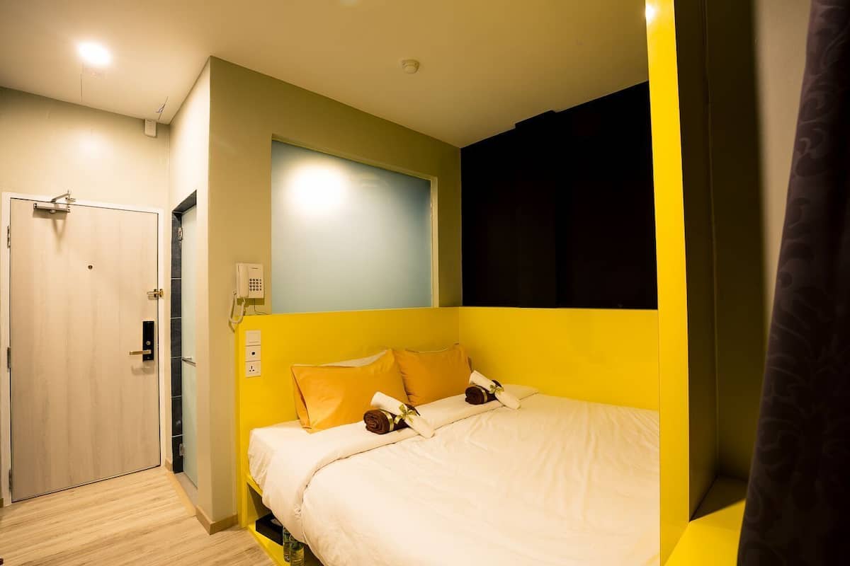 A hotel room with a bed, a door, a phone, and a light switch.